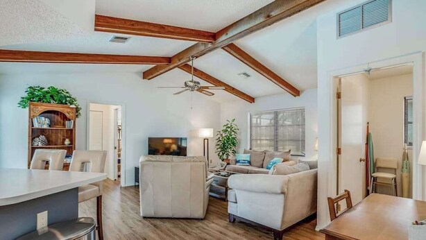 Amplia sala de estar con techo alto, vigas de madera, zona de comedor y área de descanso con sofá y sillones.