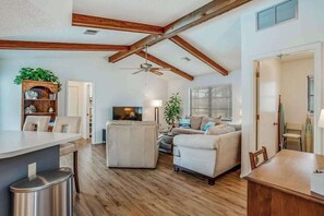 A spacious living room with a high ceiling, wooden beams, a dining area, and a seating area with a sofa and chairs. - One-level home in quiet location with private pool, central AC & open layout (Englewood)