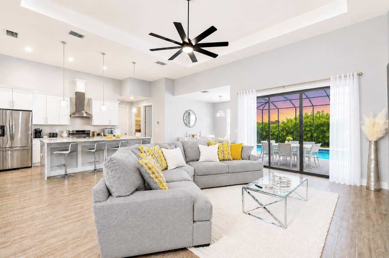 A modern living room with a grey sectional sofa, a glass coffee table, and a view of a swimming pool through large windows.