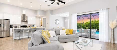 A modern living room with a grey sectional sofa, a glass coffee table, and a view of a swimming pool through large windows.