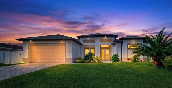 A modern two-story house with a garage, a well-maintained lawn, and a sunset sky. - Heated Pool & Hot Tub | Relaxing Southwest Florida Escape (Cape Coral)