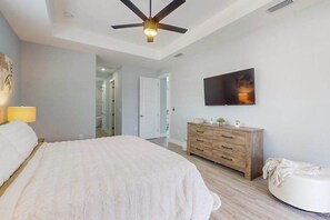 A bedroom with a bed, a ceiling fan, a wooden dresser, a TV, and a white ottoman. - Brand new, Inviting home with private pool and complimentary pool heat (Cape Coral)