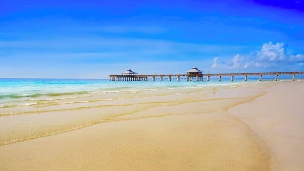 Ein Strand mit einer Mole, die sich ins Meer erstreckt, mit Bungalows über dem Wasser.