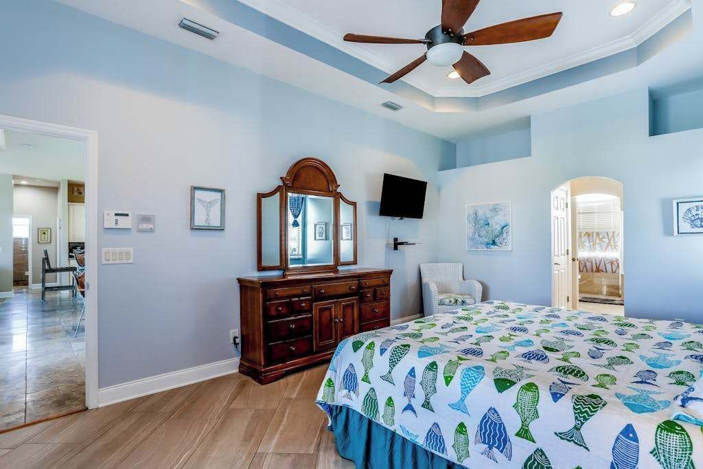 A bedroom with a bed, a ceiling fan, a dresser, a TV, and artwork on the walls.