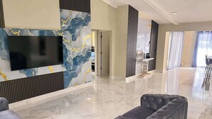 En modern hotellobby med ett marmorgolv, en stor platt-TV som är monterad på en vägg och en sittgrupp med en grå stoppad soffa.