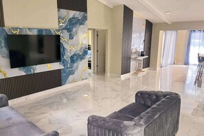 A modern hotel lobby with a marble floor, a large flat-screen TV mounted on a wall, and a seating area with a grey upholstered sofa. - Waterfront home with pool, family & dog friendly, close to river & Gulf beaches (Cape Coral)