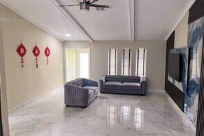 A spacious living room with a marble floor, a ceiling fan, a grey sofa, and a television mounted on the wall. - Waterfront home with pool, family & dog friendly, close to river & Gulf beaches (Cape Coral)
