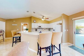 A modern kitchen with a central island, white cabinets, and a ceiling fan. - Spacious home with a private pool, pool spa, washer/dryer, & AC (Cape Coral)