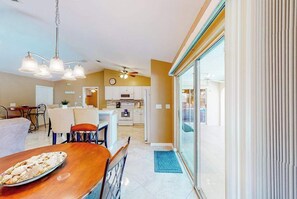 A modern kitchen with white cabinets, a dining area with a wooden table, and a large sliding glass door leading to a balcony. - Spacious home with a private pool, pool spa, washer/dryer, & AC (Cape Coral)