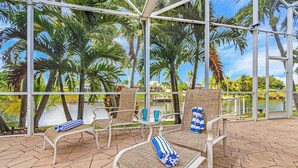 Een terras buiten met lounge stoelen en uitzicht op palmbomen en water.