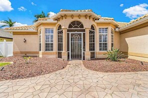 A house with a symmetrical facade, a central entrance with a glass door, and a tiled roof. - Exceptional waterfront home, refreshing pool, spa, family and dog friendly (Cape Coral)