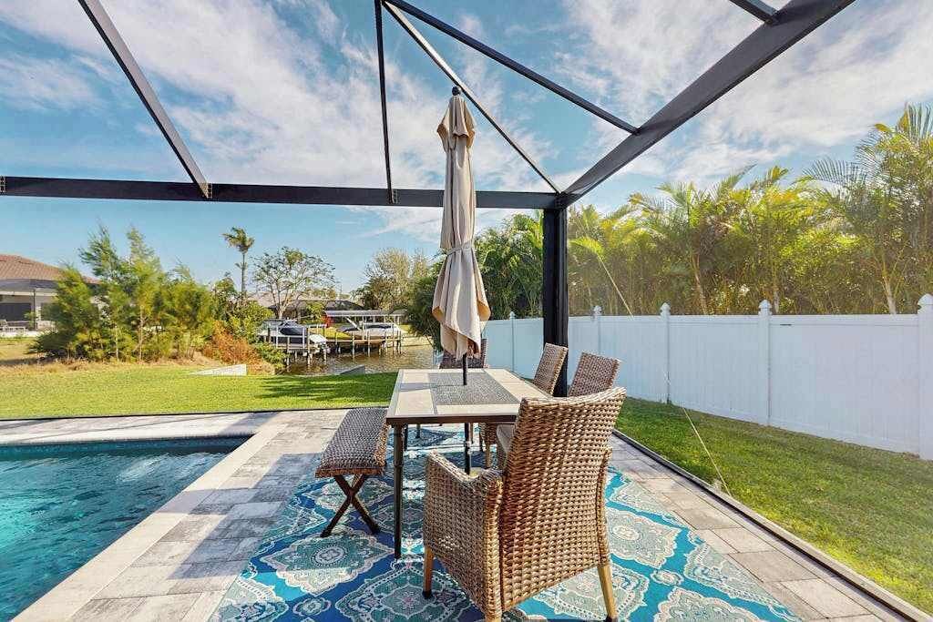 Ein überdachter Außenbereich mit Pool, einem Tisch mit Stühlen und Blick auf einen Garten.