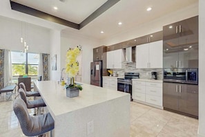 A modern kitchen with a central island, white cabinetry, and stainless steel appliances. - Modern canal-front luxury with pool, patio, grill, dock, Ping-Pong, AC, & WiFi (Cape Coral)