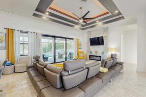 A modern living room with a sectional sofa, a flat-screen TV, and a ceiling fan. - Modern canal-front luxury with pool, patio, grill, dock, Ping-Pong, AC, & WiFi (Cape Coral)