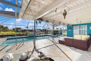 A covered pool area with a lounge chair, a small table, and a view of the outdoors. - Waterfront retreat with pool, arcade game, family friendly (Cape Coral)