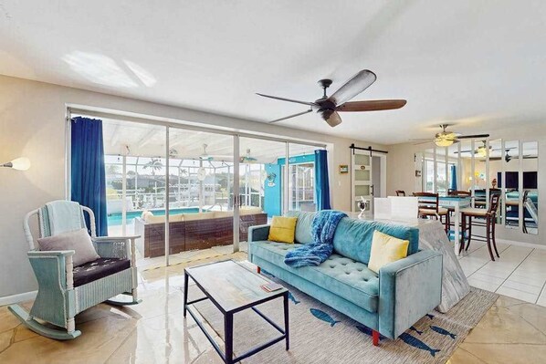 A living room with a sofa, a rocking chair, a coffee table, and a ceiling fan. - Waterfront retreat with pool, arcade game, family friendly (Cape Coral)