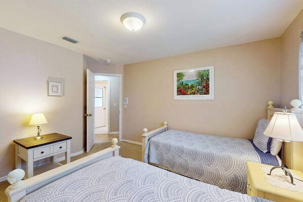 A bedroom with two beds, a bedside table with a lamp, a door leading to another room, and a framed picture on the wall. - Exclusive Wellington Lakes Waterfront Home with Private Pool, Lake Views, & WiFi (Fort Myers)