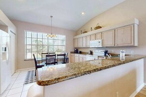 A modern kitchen with a large island, white cabinetry, and a window providing natural light. - Exclusive Wellington Lakes Waterfront Home with Private Pool, Lake Views, & WiFi (Fort Myers)
