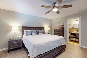 Ein Schlafzimmer mit Bett, Nachttischen, Deckenventilator und einem durchgehenden Türspalt sichtbaren Badezimmer.
