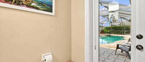 A room with a beach painting, a door leading to a pool area, and a trash bin.