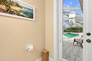 Ein Zimmer mit einem Strandbild, einer Tür zu einem Poolbereich und einem Mülleimer.
