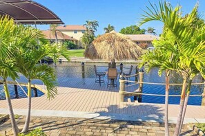 Área de piscina com guarda-sol de palha, palmeiras e deck de madeira.