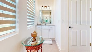 Un pasillo con una mesa de vidrio y una silla, una puerta blanca y una zona de cocina con armarios y una encimera.