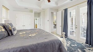 A bedroom with a bed, a ceiling fan, a door, and a view to a balcony. - Beautiful home with private pool, waterfront views & home theater (Cape Coral)