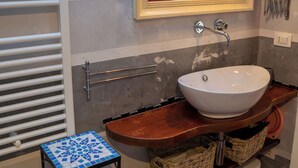 Un baño con lavamanos blanco, un espejo, toallero y una mesita con cestas.