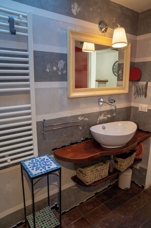 Un bagno con lavandino bianco, uno specchio, un portasciugamani e un piccolo tavolo con cesti.