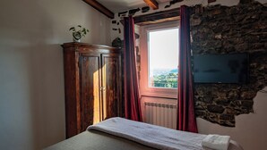 Un dormitorio con cama, armario, ventana con cortinas y pared de piedra.
