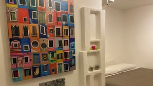 Un dormitorio con un cuadro de colores, una cama y un estante blanco.