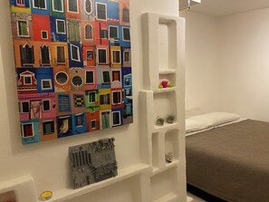 Una camera da letto con un'opera d'arte colorata al muro, un letto e un mobiletto bianco.
