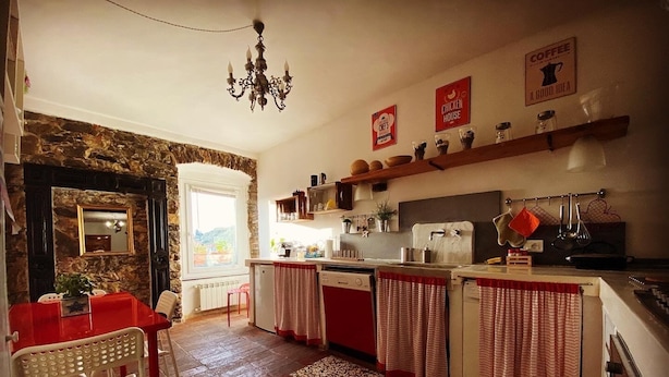 Una cocina con pared de piedra, una araña, una mesa roja y vistas al exterior.