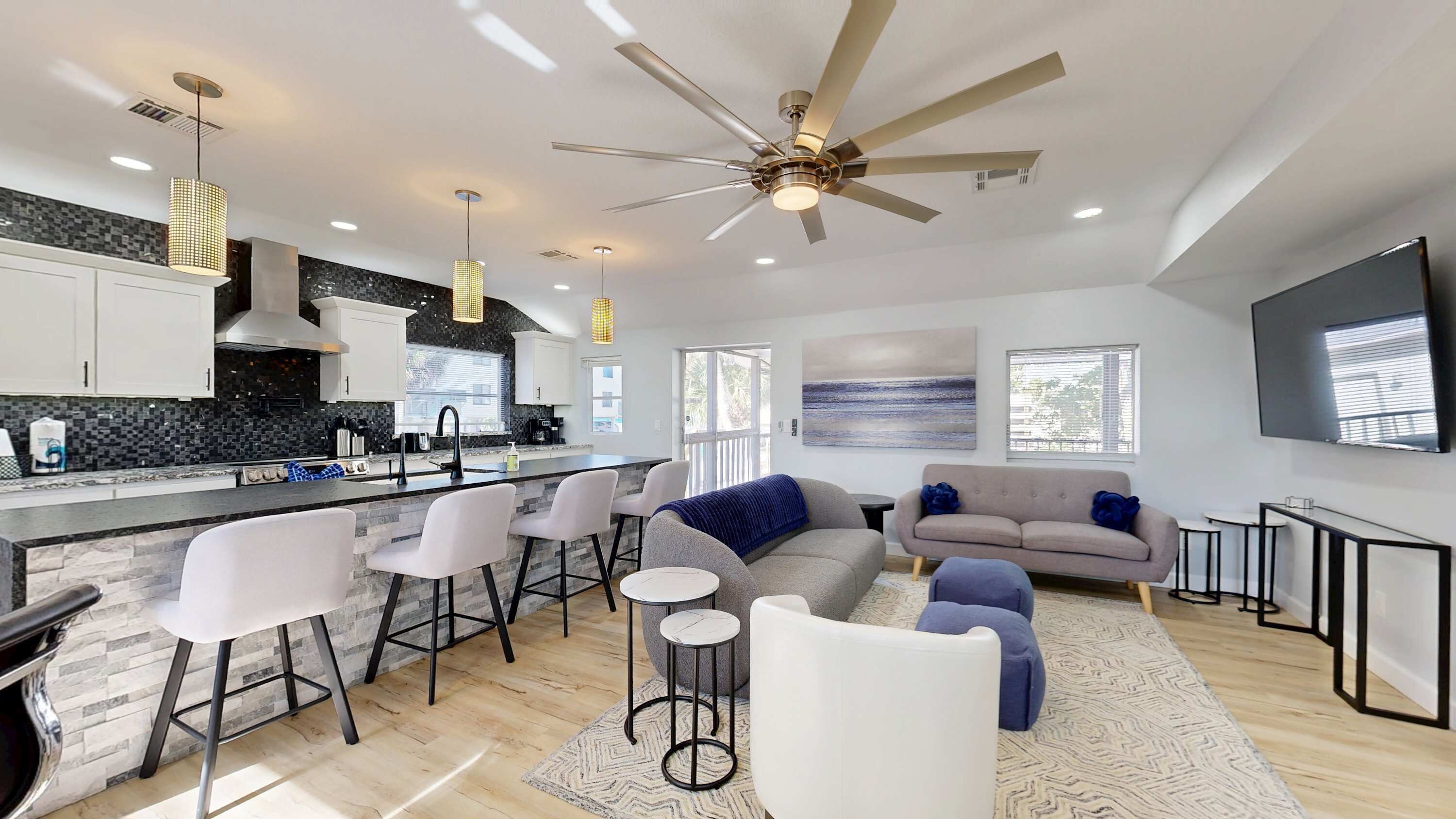 A modern kitchen with a central island, bar stools, a sofa, and a ceiling fan.