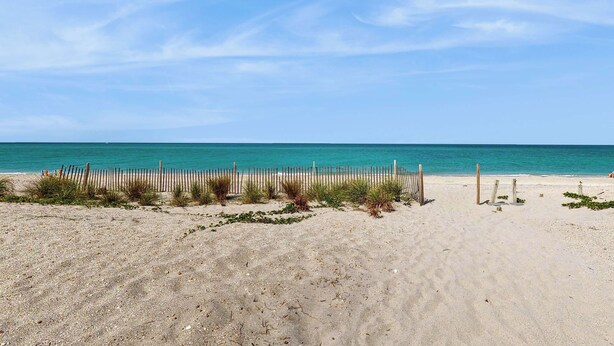 Ein sandiger Strand mit einer Holzlattenzaun und einem wolkenlosen, blauen Himmel.