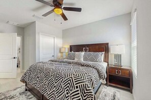 Een slaapkamer met een bed, nachtkastje, lamp, plafondventilator en een deur.
