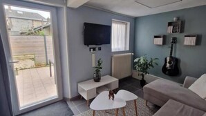 A living room with a sofa, a coffee table, a TV, a guitar, and a plant. - Cosy house with terrace near Rouen - Peace and comfort 10 min from the center (Amfreville-la-Mi-Voie)