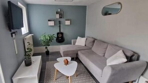 A living room with a grey sofa, a white coffee table, a TV mounted on the wall, and a guitar. - Cosy house with terrace near Rouen - Peace and comfort 10 min from the center (Amfreville-la-Mi-Voie)