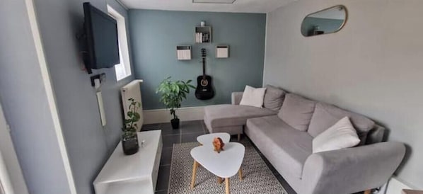 A living room with a grey sofa, a white coffee table, a TV mounted on the wall, and a guitar.