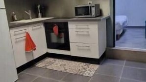 A compact kitchen with white cabinets, a microwave, and a small rug. - Cosy house with terrace near Rouen - Peace and comfort 10 min from the center (Amfreville-la-Mi-Voie)