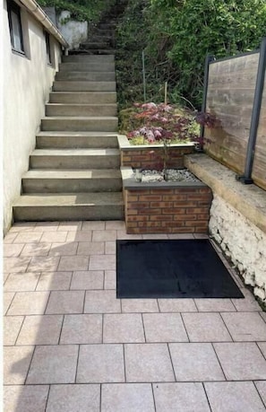A set of stone steps leading up to a brick planter with a small tree, surrounded by a stone wall and a wooden fence.