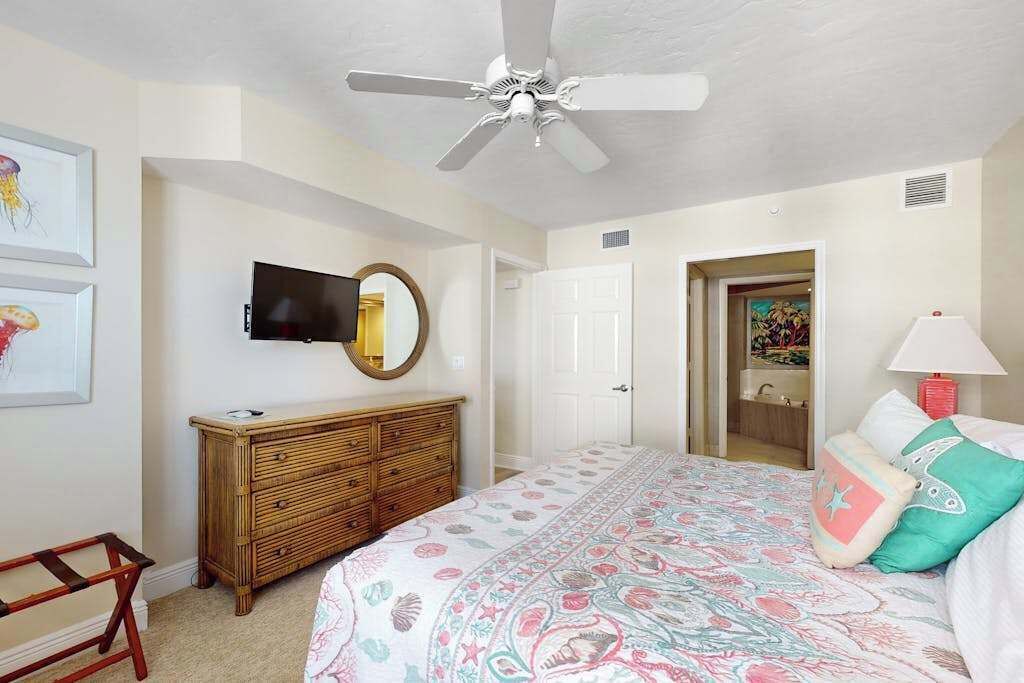 Ein Schlafzimmer mit Bett, Kommode, Fernseher, Deckenventilator und Bildern an der Wand.