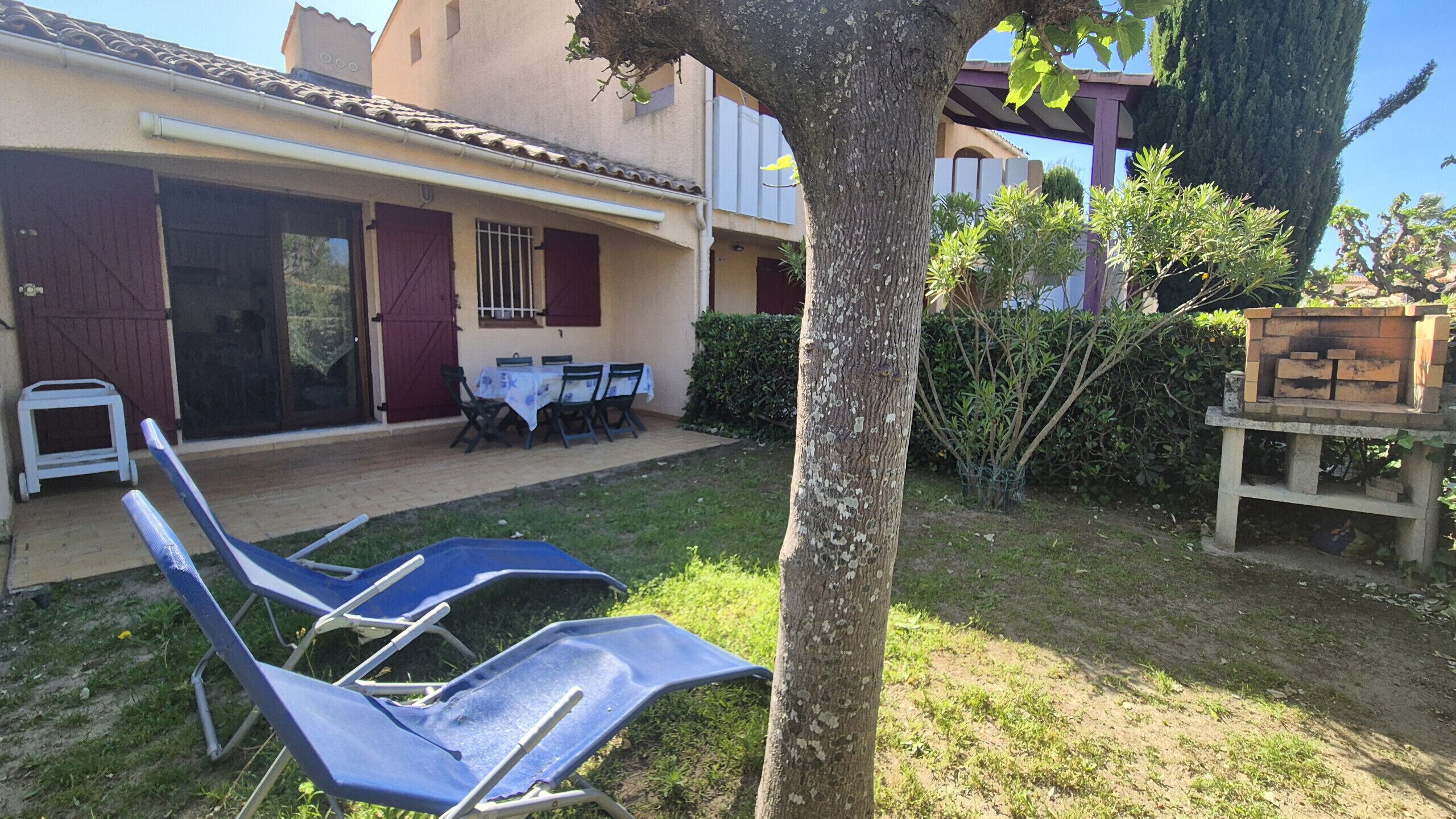 Een terras met twee loungestoelen, een tafel, stoelen, een klein witte kar en een bakoven van baksteen.