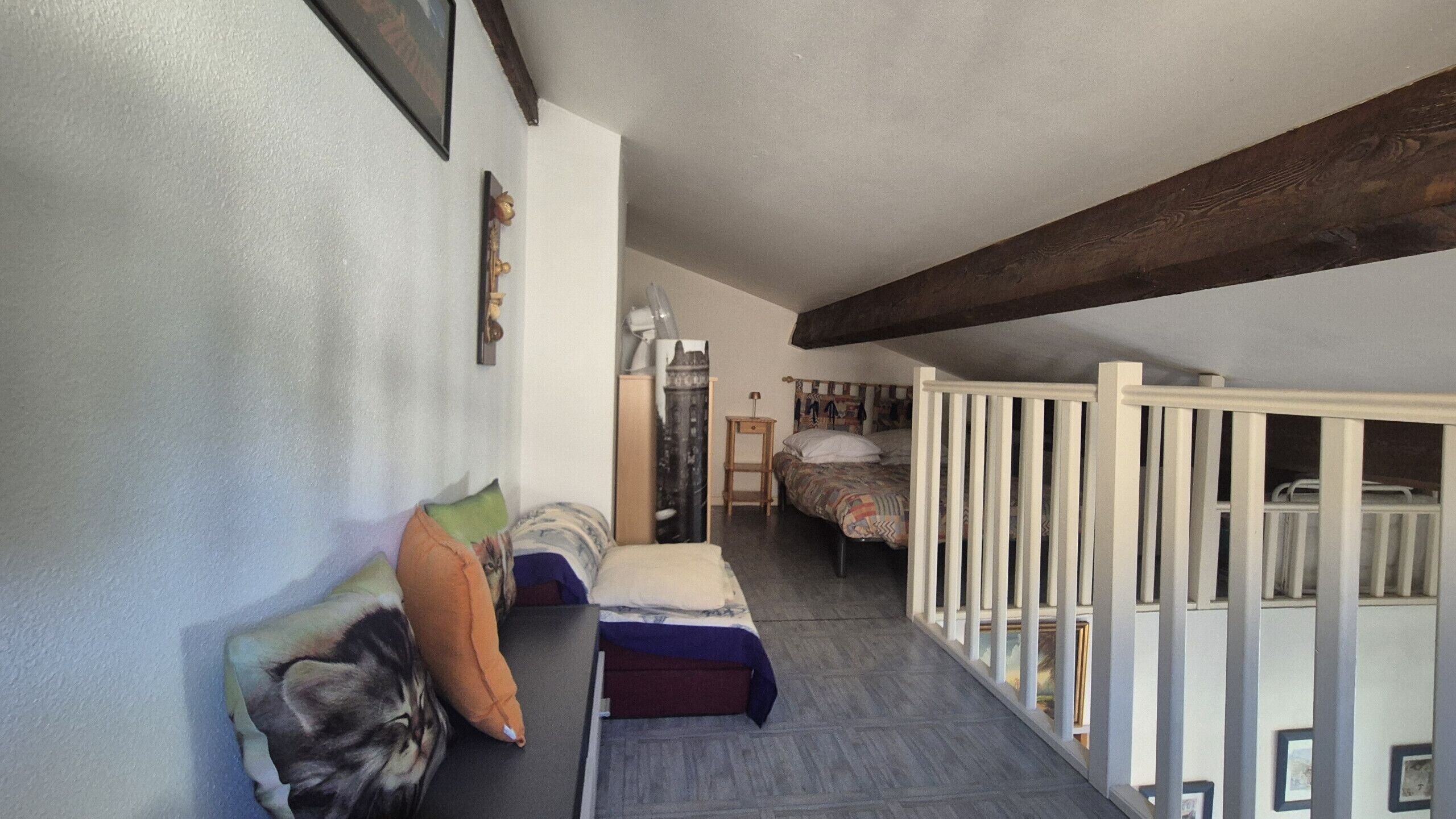 A narrow hallway with a bed on the right, a small table, and a chair.