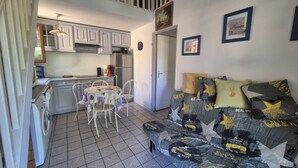 Een knus woongedeelte met kitchenette, een eethoek en een bank met opvallende kussens.