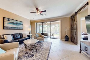 A living room with a sofa, coffee table, and a ceiling fan. - Spacious home with enclosed lanai, WiFi, AC, WD, pool, tennis court, & gym (Estero)