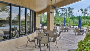 An outdoor patio area with tables and chairs, large windows, and a pool view. - Spacious home with enclosed lanai, WiFi, AC, WD, pool, tennis court, & gym (Estero)