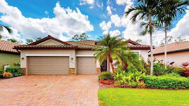 A residential house with a garage, a well-maintained lawn, and tropical plants. - Spacious home with enclosed lanai, WiFi, AC, WD, pool, tennis court, & gym (Estero)