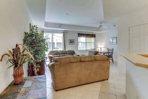 A spacious living area with a beige sofa, a dining table, and a large plant. - Family-Friendly Townhouse with Shared Pool - Close to Golf & Beach (Fort Myers)